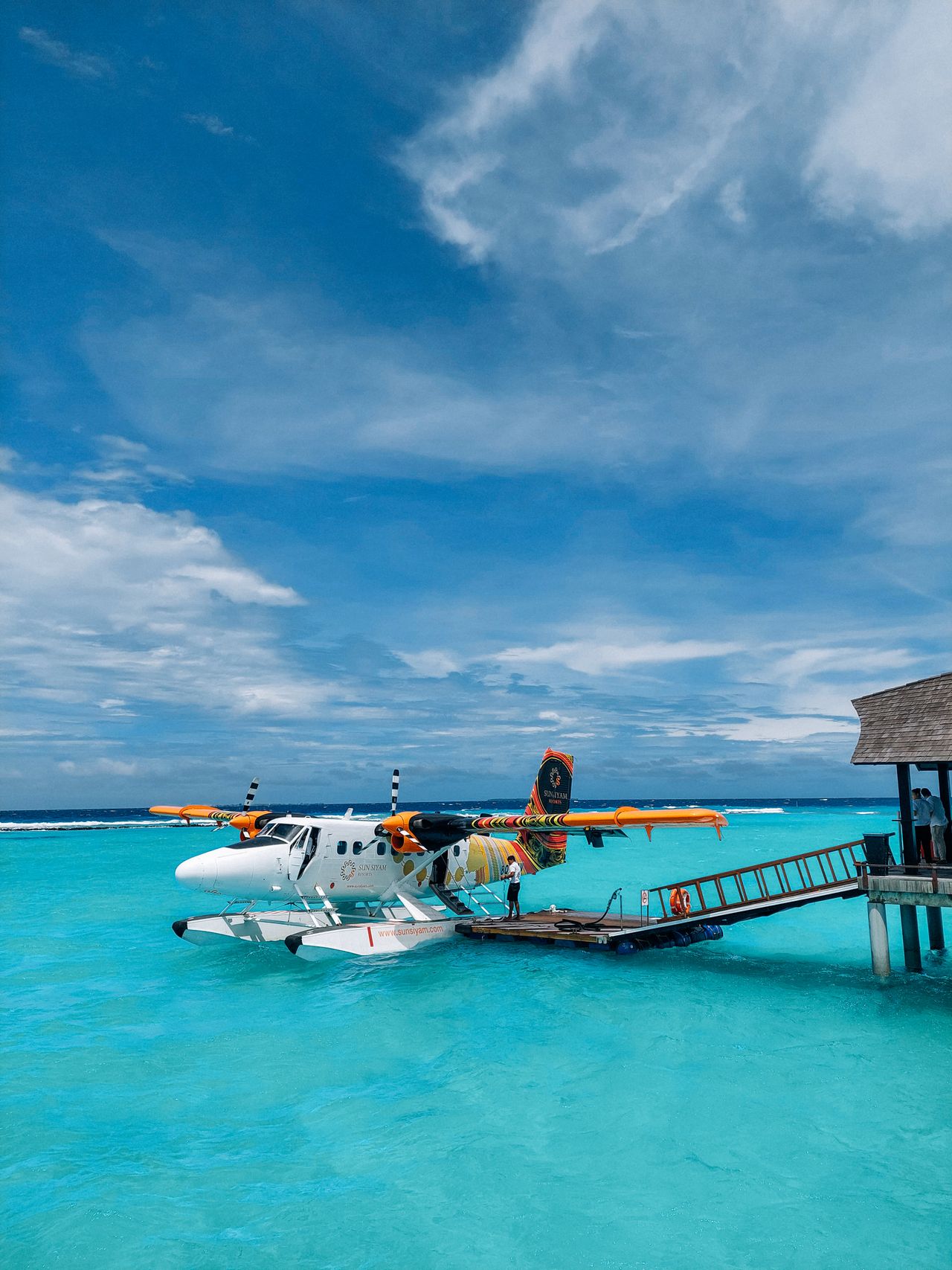 A seaplane moored at a wooden jetty over turquoise water under a bright sky