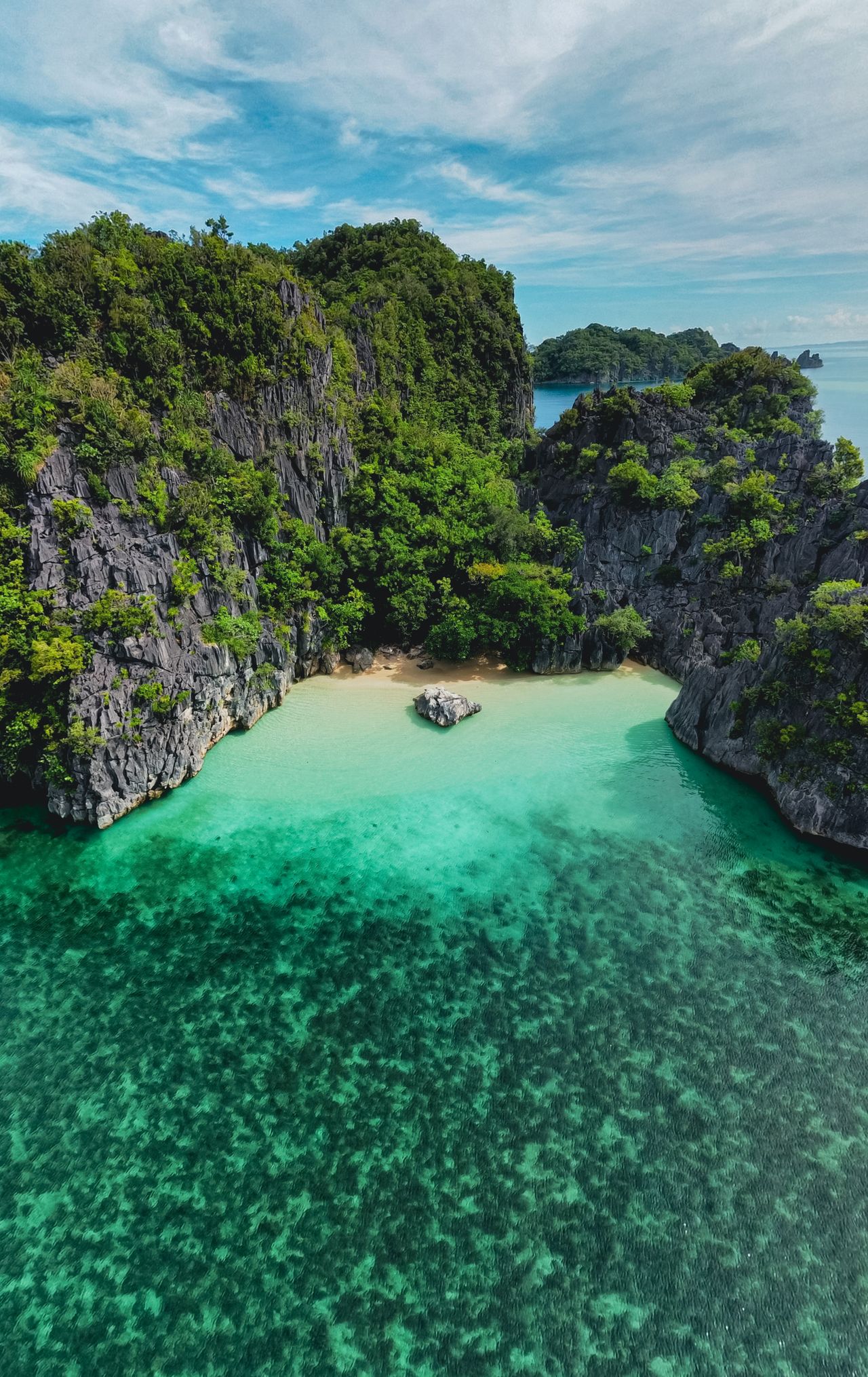 A sheltered turquoise lagoon and small beach enclosed by green limestone cliffs