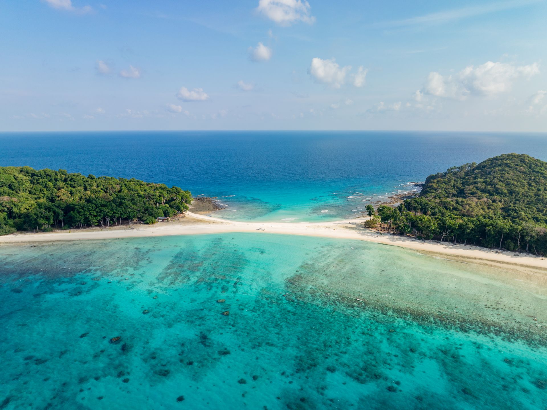 Aerial view of a white sandbar joining two forested islands across a turquoise reef