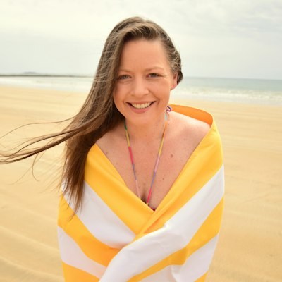 A smiling woman wrapped in a striped beach towel on the sand