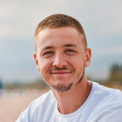 A smiling man in a white T-shirt with the beach behind him