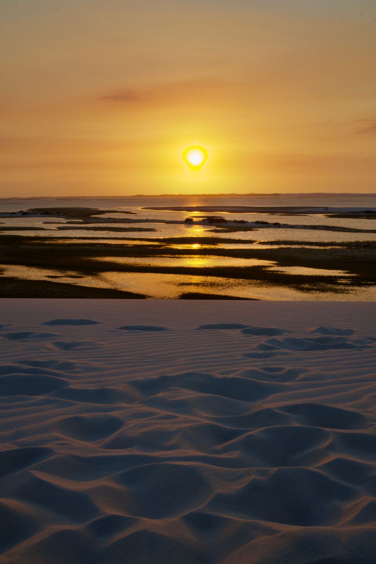The sun setting over tidal sandbanks, with rippled sand in the foreground